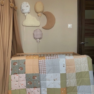 Könnte beinhalten: Eine Patchwork-Babydecke mit Waldmotiv mit Igeln, Pilzen und Blättern in Grün-, Braun- und Beigetönen. Die Decke ist aus weichem, gestepptem Stoff gefertigt und perfekt für ein Kinderzimmer oder Babyzimmer.