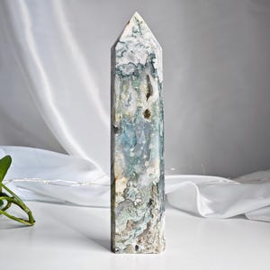 May include: A green, white, and blue agate crystal point, also known as a wand or obelisk. The crystal is polished and has a natural, organic shape.
