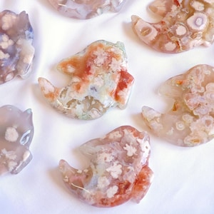 May include: A collection of seven agate fish carvings in various shades of pink, white, and brown. The fish are all carved in a similar style, with a rounded body and a long, flowing tail. The agate is translucent, and the carvings show the natural patterns and colors of the stone.