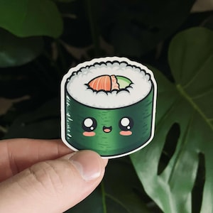 May include: A green and white cartoon sushi roll with a smiling face. The sushi roll has a pink and green filling.