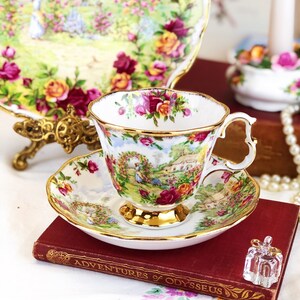 K&ouml;nnte beinhalten: Eine wei&szlig;e Teetasse und Untertasse mit floralem Muster und goldener Verzierung. Die Teetasse und Untertasse stehen auf einem roten Buch mit dem Titel "Die Abenteuer des Odysseus".