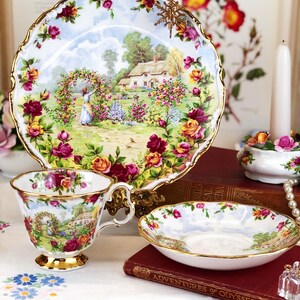 K&ouml;nnte beinhalten: Ein Vintage-Teetassen- und Untertassen-Set mit einem Blumenmuster. Das Set zeigt eine Cottage-Szene mit einer Frau, die sich um einen Rosengarten k&uuml;mmert. Die Teetasse und die Untertasse sind mit Gold verziert.