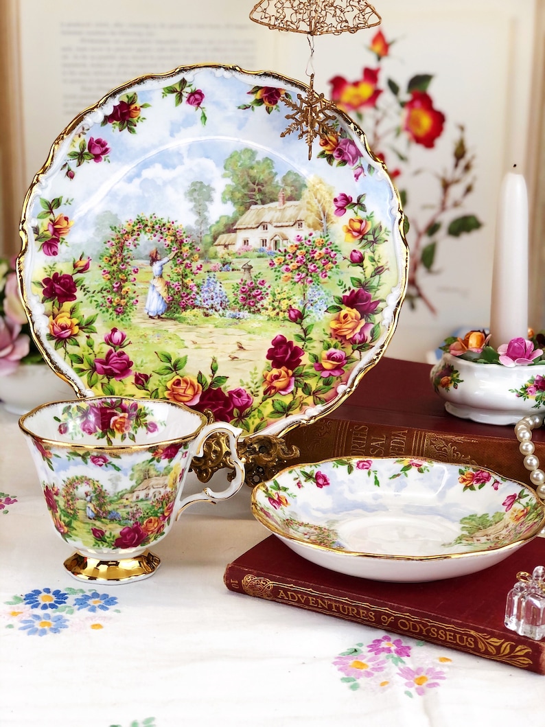 K&ouml;nnte beinhalten: Ein Vintage-Teetassen- und Untertassen-Set mit einem Blumenmuster. Das Set zeigt eine Cottage-Szene mit einer Frau, die sich um einen Rosengarten k&uuml;mmert. Die Teetasse und die Untertasse sind mit Gold verziert.