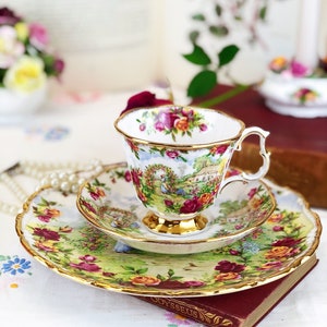 K&ouml;nnte beinhalten: Ein Vintage-Teetassen- und Untertassen-Set mit einem Blumenmuster. Tasse und Untertasse haben einen goldenen Rand und ein zartes Blumenmuster mit rosa, roten und gelben Rosen. Das Set steht auf einem Buch mit dem sichtbaren Wort "Odysseus".