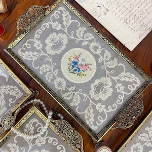 Pode incluir: Bandejas retangulares vintage com molduras douradas ornamentadas e inserções de renda branca. Cada bandeja apresenta um design floral bordado central em uma moldura circular. As bandejas têm alças decorativas.
