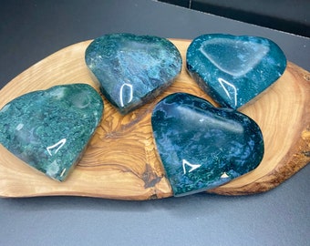 May include: Four green and blue heart-shaped polished stones on a wooden surface. The stones have a swirling pattern and white veins.
