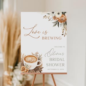 May include: A white sign on a copper easel with the text "Love is Brewing" in brown script. The sign welcomes guests to Olivia's Bridal Shower, with a coffee cup graphic and floral accents. The date is September 15, 20XX.
