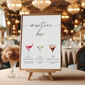 May include: A framed sign with the words "martini bar" in elegant script. The sign displays watercolor illustrations of three martini cocktails: French, Dry, and Espresso. The sign is displayed on a small wooden easel.