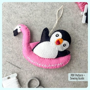 Puede incluir: Un flotador de flamenco rosa de fieltro con un pingüino encima. El pingüino es blanco con la cabeza y las alas negras. El flotador tiene costuras blancas alrededor de los bordes. Las palabras "PDF Pattern + Sewing Guide" están en la esquina inferior derecha de la imagen.