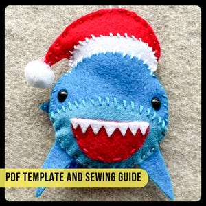 May include: A blue felt shark wearing a red and white Santa hat. The shark has a white mouth with red teeth and black eyes. The shark is a Christmas ornament.