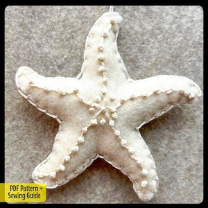 Op de afbeelding: Een witte viltsterrenornament met witte stiksels en witte kralen rond de randen. De ster is opgehangen aan een wit touwtje.