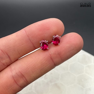 May include: A pair of silver stud earrings with oval-shaped ruby gemstones.