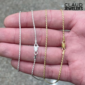 May include: Three gold and silver rope chains on a hand. The chains are all the same length and have a clasp at the end.