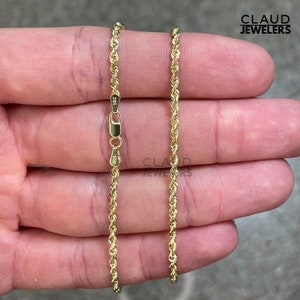 May include: A gold rope chain necklace with a clasp. The chain is 14k gold and is shown on a hand.