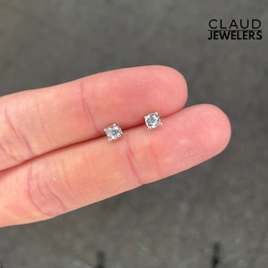 May include: A pair of silver stud earrings with small, clear round stones.