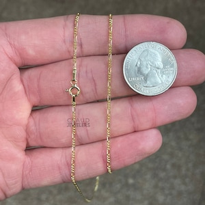 May include: A gold chain necklace with a lobster clasp. The chain is about 18 inches long and is made of a fine, delicate design. The chain is shown next to a US quarter for size comparison.