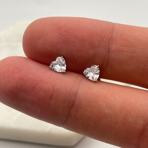 May include: A pair of silver heart-shaped stud earrings with clear cubic zirconia stones.