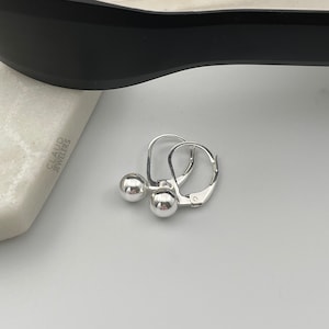 May include: A pair of silver hoop earrings with small ball accents. The earrings are simple and elegant.