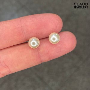 May include: A pair of pearl stud earrings. The earrings are white and round.