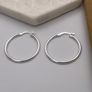 May include: A pair of silver hoop earrings. The earrings are simple and elegant, with a smooth, polished finish.