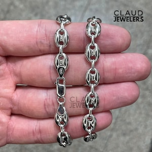 May include: Two silver chains with a curb link design. The chains are on a hand and the chain on the left has a 925 stamp.