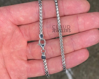 May include: A silver chain necklace with a lobster clasp. The chain is a box style with a fine, delicate design. The chain is shown on a hand, and the text "CLAUD JEWELERS" is visible in the background.