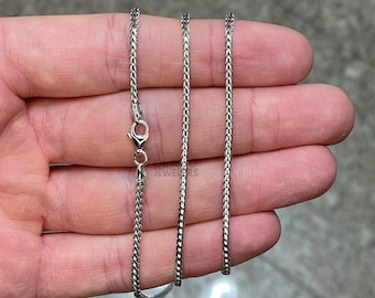 May include: A silver chain necklace with a lobster clasp. The chain is a box chain style and is shown on a hand.