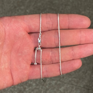 May include: A silver adjustable chain necklace with a sliding clasp. The chain is made of a delicate, braided design.