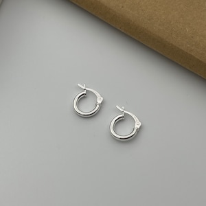 May include: A pair of silver hoop earrings. The earrings are small and simple, with a smooth finish.