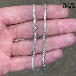 May include: A silver chain necklace with a box clasp. The chain is made of small, square links.