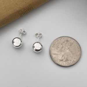 May include: A pair of silver stud earrings with round, smooth, silver balls. The earrings are shown next to a US quarter for size comparison.