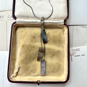 Op de afbeelding: Een zilveren ketting met drie rechthoekige hangers van parelmoer. De ketting ligt in een fluwelen juwelendoos.