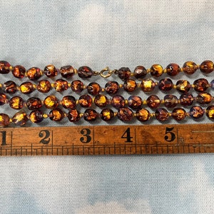 May include: A multi-strand necklace made of brown glass beads with gold flecks. The beads are approximately 1 inch in diameter and the necklace measures 5 inches long.