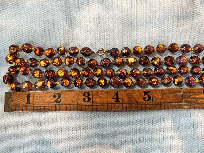 May include: A multi-strand necklace made of brown glass beads with gold flecks. The beads are approximately 1 inch in diameter and the necklace measures 5 inches long.