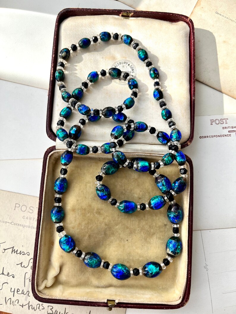 May include: A blue and green glass bead necklace with black beads. The necklace is in a velvet-lined jewelry box.