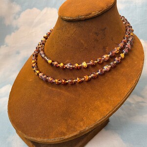 May include: A double strand necklace made of iridescent glass beads with gold flecks. The beads are round and have a textured surface. The necklace is displayed on a brown velvet mannequin.