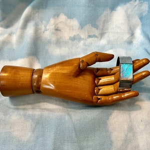 Puede incluir: Un brazalete de plata con una incrustación de ala de mariposa azul iridiscente. El brazalete está en un maniquí de mano de madera.