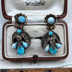 May include: Vintage earrings with turquoise-colored stones and ornate metalwork. The earrings are displayed in a brown jewelry box. The box has a cream-colored interior and the text "O'Keefe Jeweller Athlone" is visible.