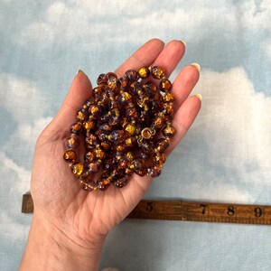 May include: A long necklace made of iridescent glass beads with a gold metallic finish. The beads are round and have a textured surface. The necklace is approximately 18 inches long.
