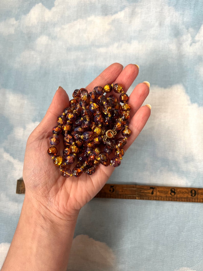 May include: A long necklace made of iridescent glass beads with a gold metallic finish. The beads are round and have a textured surface. The necklace is approximately 18 inches long.