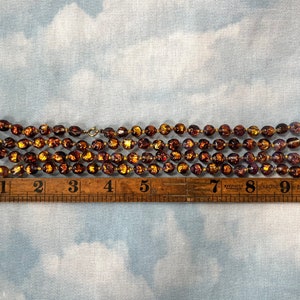 May include: A strand of brown glass beads with gold flecks. The beads are approximately 1/2 inch in diameter. The strand is about 9 inches long.
