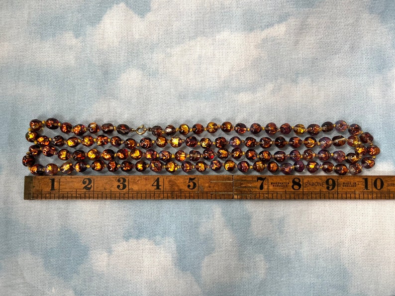 May include: A strand of brown glass beads with gold flecks. The beads are approximately 1/2 inch in diameter. The strand is about 9 inches long.