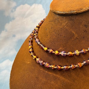May include: A double strand necklace made of purple and gold glass beads. The beads are round and have a metallic sheen.