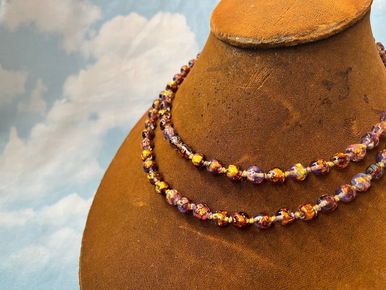 May include: A double strand necklace made of purple and gold glass beads. The beads are round and have a metallic sheen.