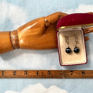 May include: A pair of gold clip-on earrings with black and white agate spheres. The earrings are in a red velvet box.