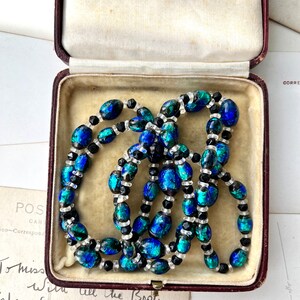 May include: A vintage necklace made of blue and green iridescent glass beads with black and clear spacer beads. The necklace is in a red velvet jewelry box.