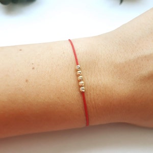 Peut inclure: Un bracelet en cordon rouge avec cinq petites perles dorées.