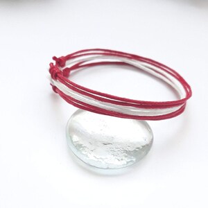 May include: Red and white braided friendship bracelet with multiple strands of cord.