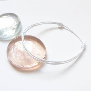 Puede incluir: Un brazalete de cuerda blanco con un cierre simple de nudo. El brazalete está hecho de una cuerda fina y duradera y es ajustable para adaptarse a la mayoría de las muñecas.