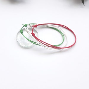 May include: Three friendship bracelets in red, white, and green colors. The bracelets are made of thin cord and are tied together in a knot.